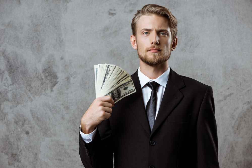 Poslovni čovjek u odijelu drži snop novčanica – simbol klijenata koji imaju novac i traže vrijednost